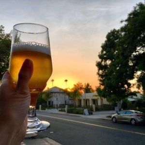 hand holding a glass of beer with sunset in background